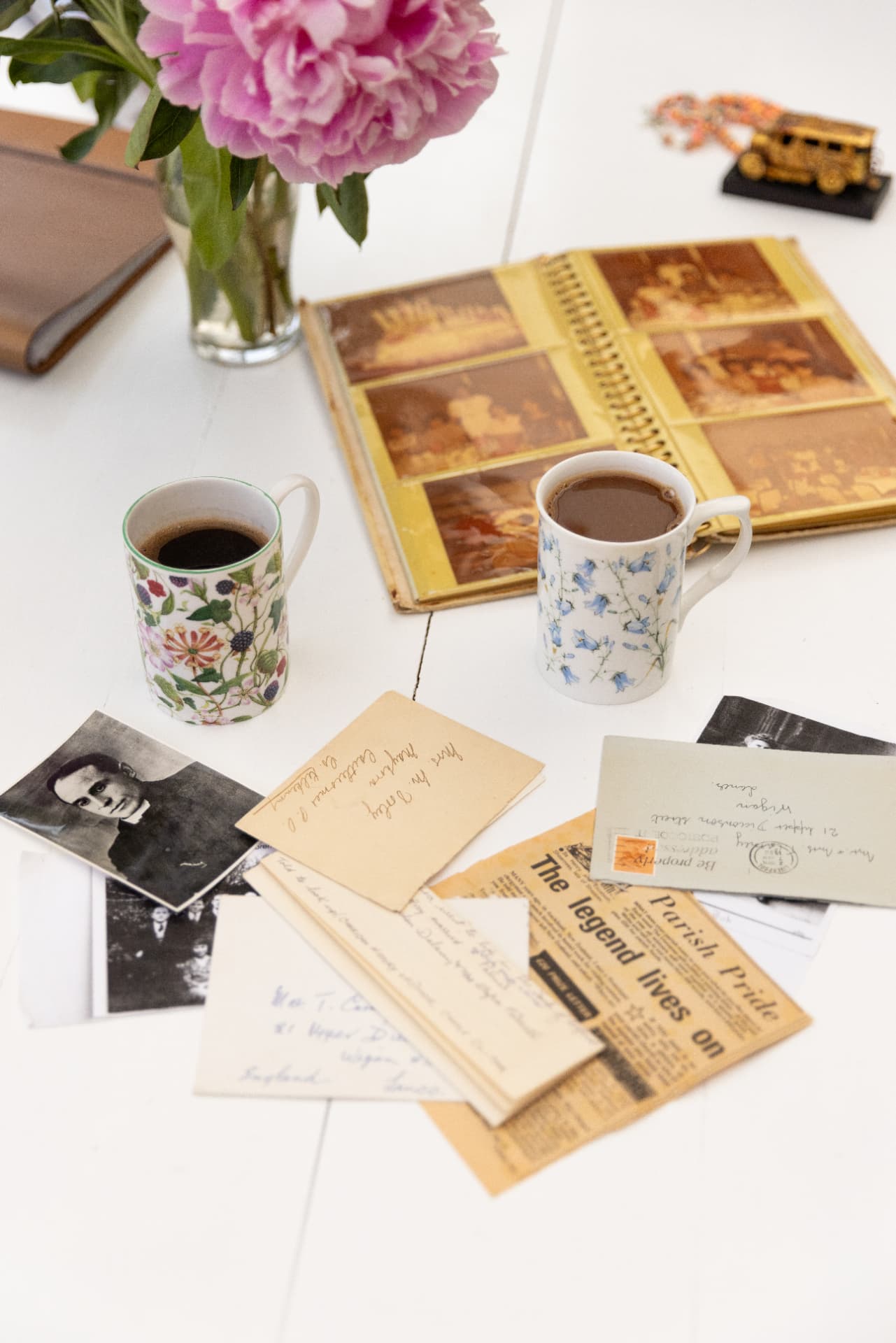 Family photo album, letters and newspaper clippings spread across a table with mugs of coffee