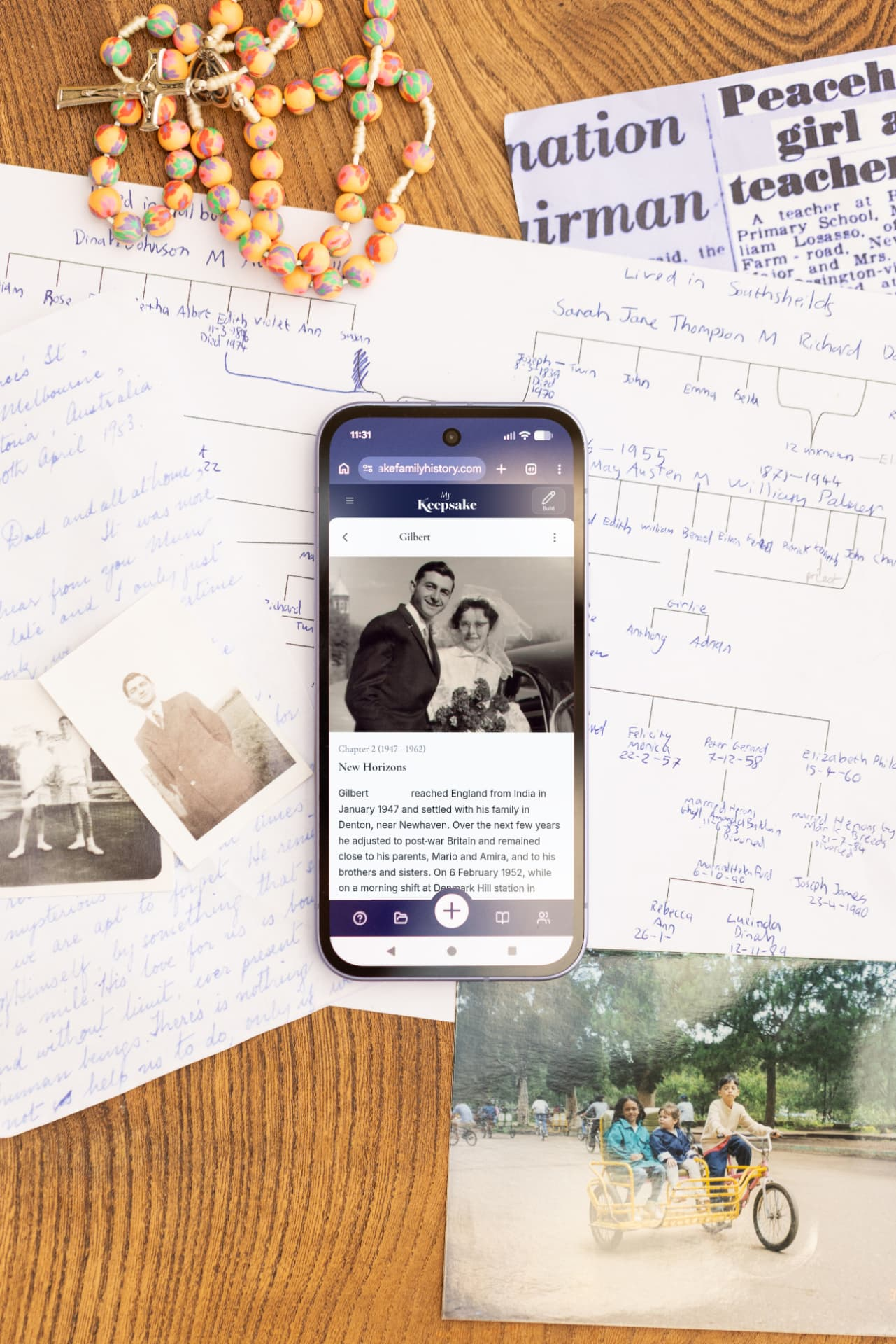Handwritten family trees, old photographs and newspaper clippings around a phone showing a Keepsake life story chapter