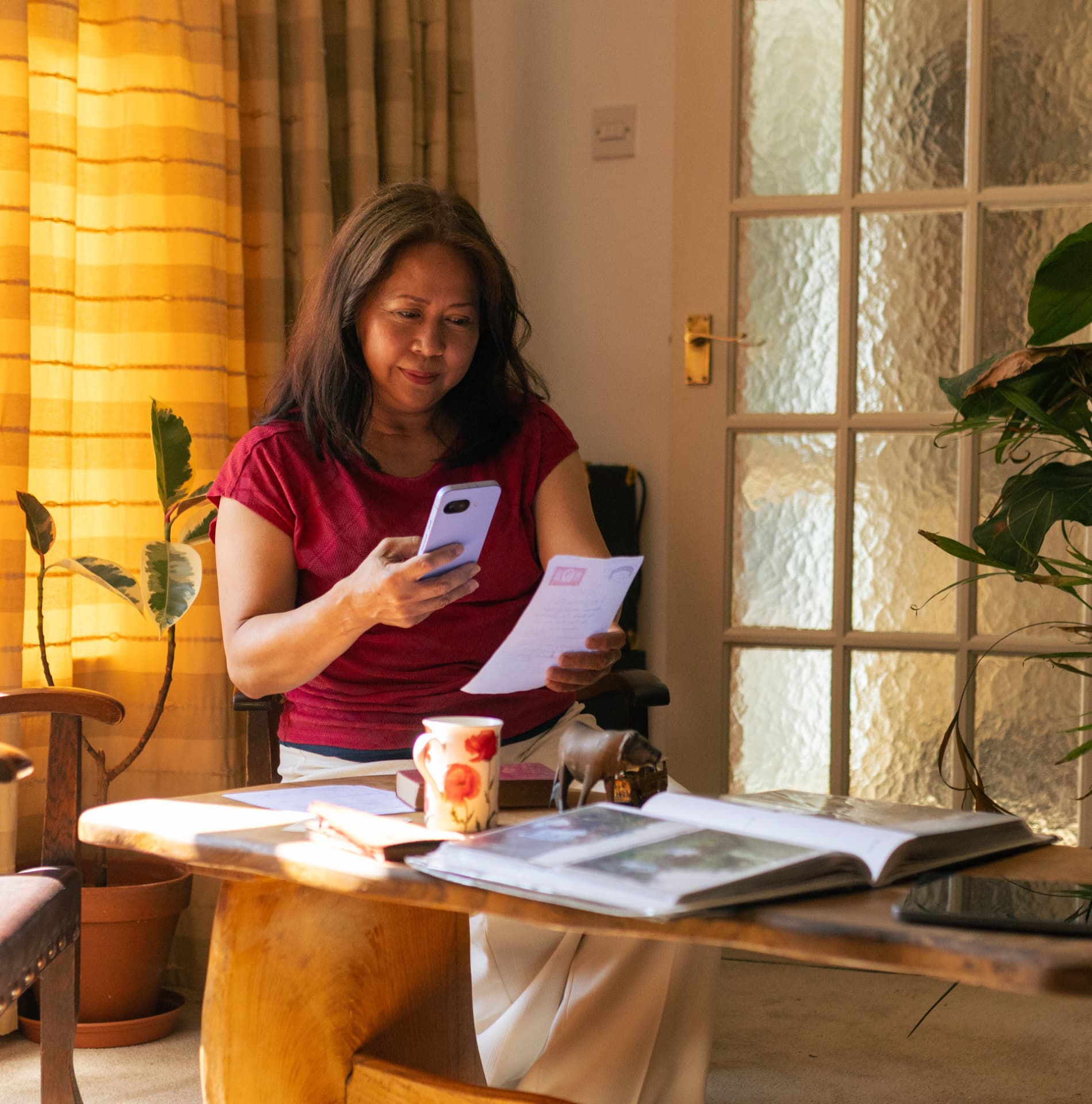 A woman photographing a handwritten letter with her phone at a sunlit table